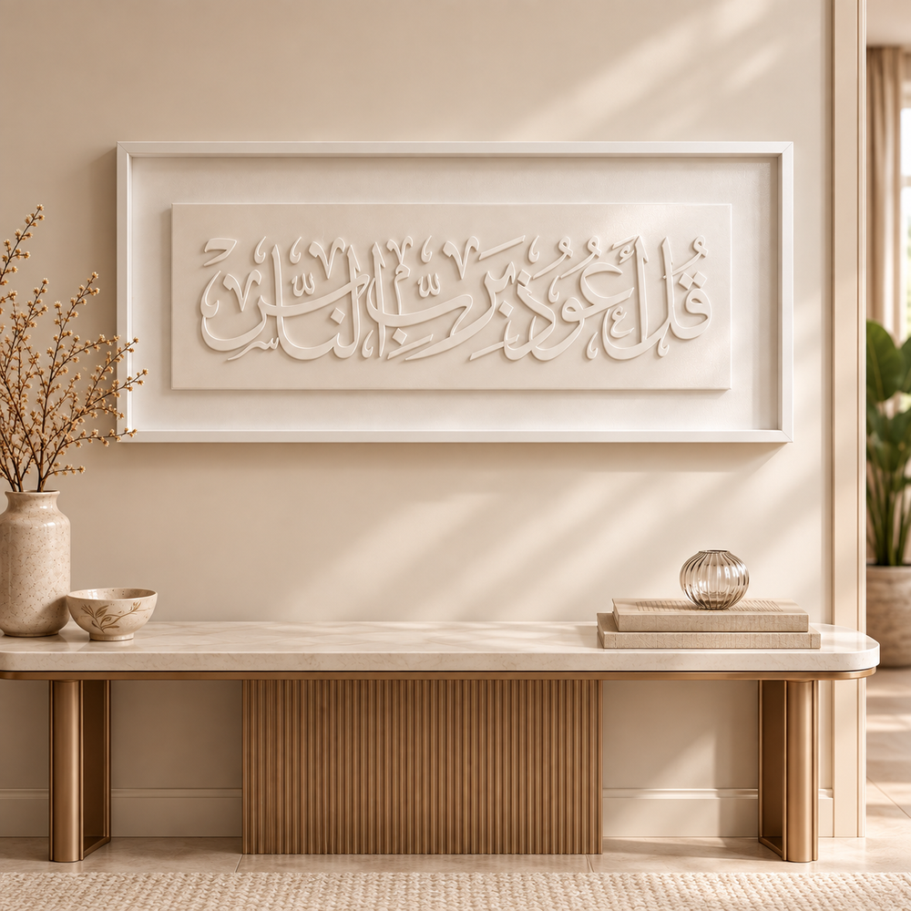 A rectangular framed Islamic calligraphy for Qul auzu bi rabbin naas wall art piece in a warm beige tone, displayed in a modern, minimalist entryway above a marble-topped console table with wooden legs.