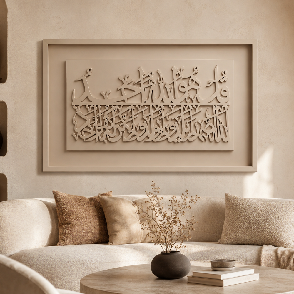 A beige framed wall art piece with carved Arabic calligraphy hangs above a cream-colored sofa in a warm, modern living room setting.