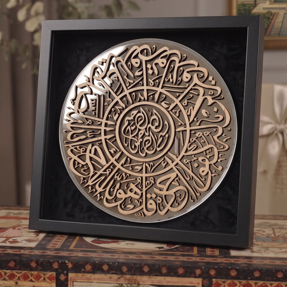A square black shadow box display featuring a circular metallic Islamic calligraphy plaque with Arabic script, set on a decorative table with traditional artwork in the background.