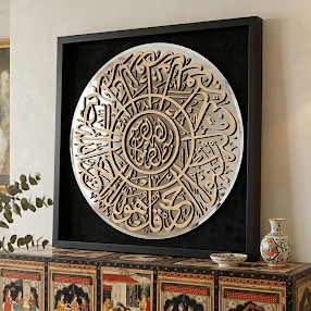 Large square black-framed wall art featuring an intricate circular Arabic calligraphy design in light beige against a black background, displayed in a styled interior room above a decorative cabinet.