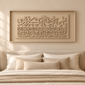 A beige framed Islamic wall art piece with intricate Arabic calligraphy, displayed above a neatly made bed in a warm, modern bedroom setting.