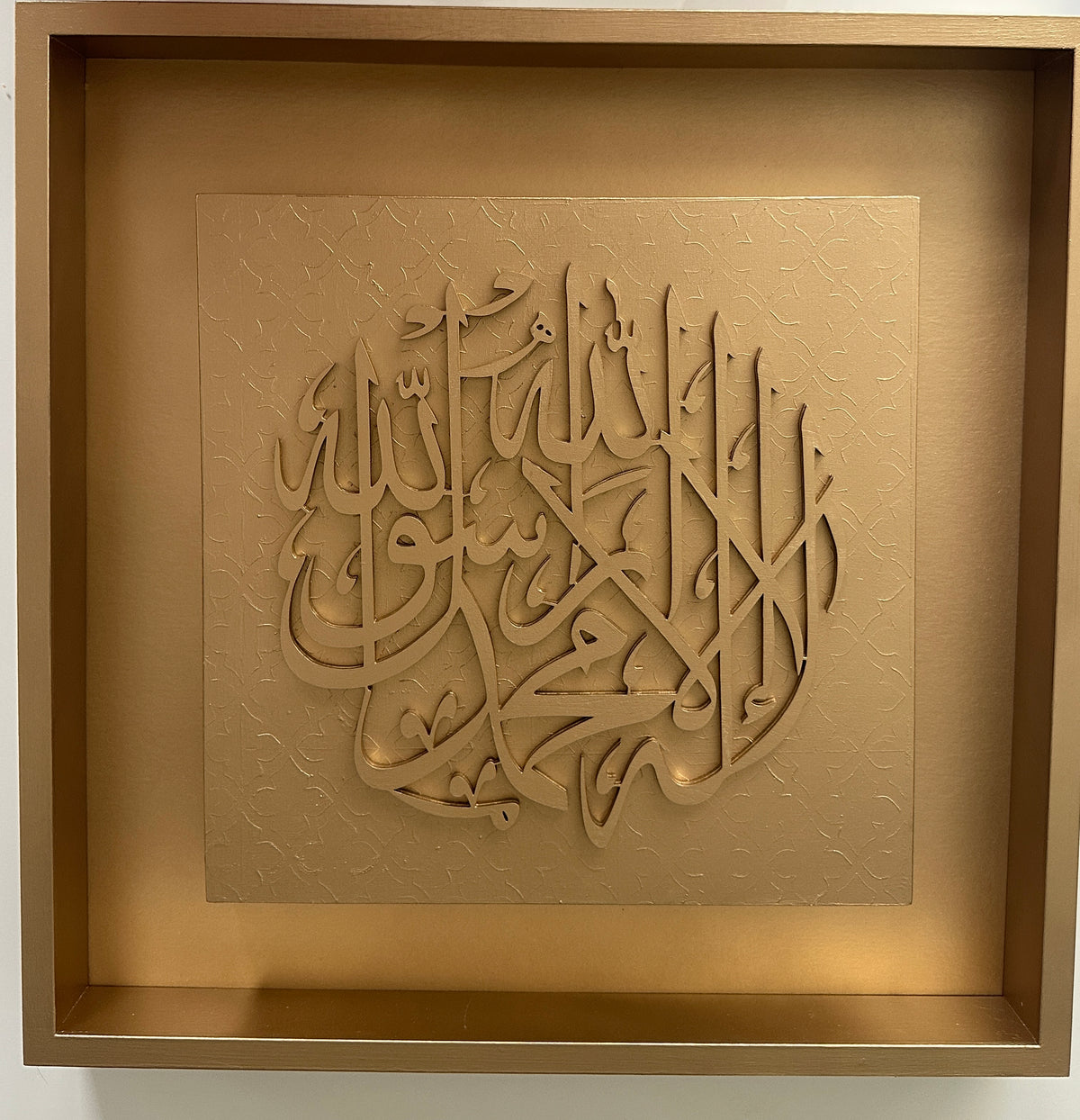 Square framed Islamic wall art featuring elegant Arabic calligraphy in a metallic gold finish, mounted on a textured gold panel within a matching gold frame.