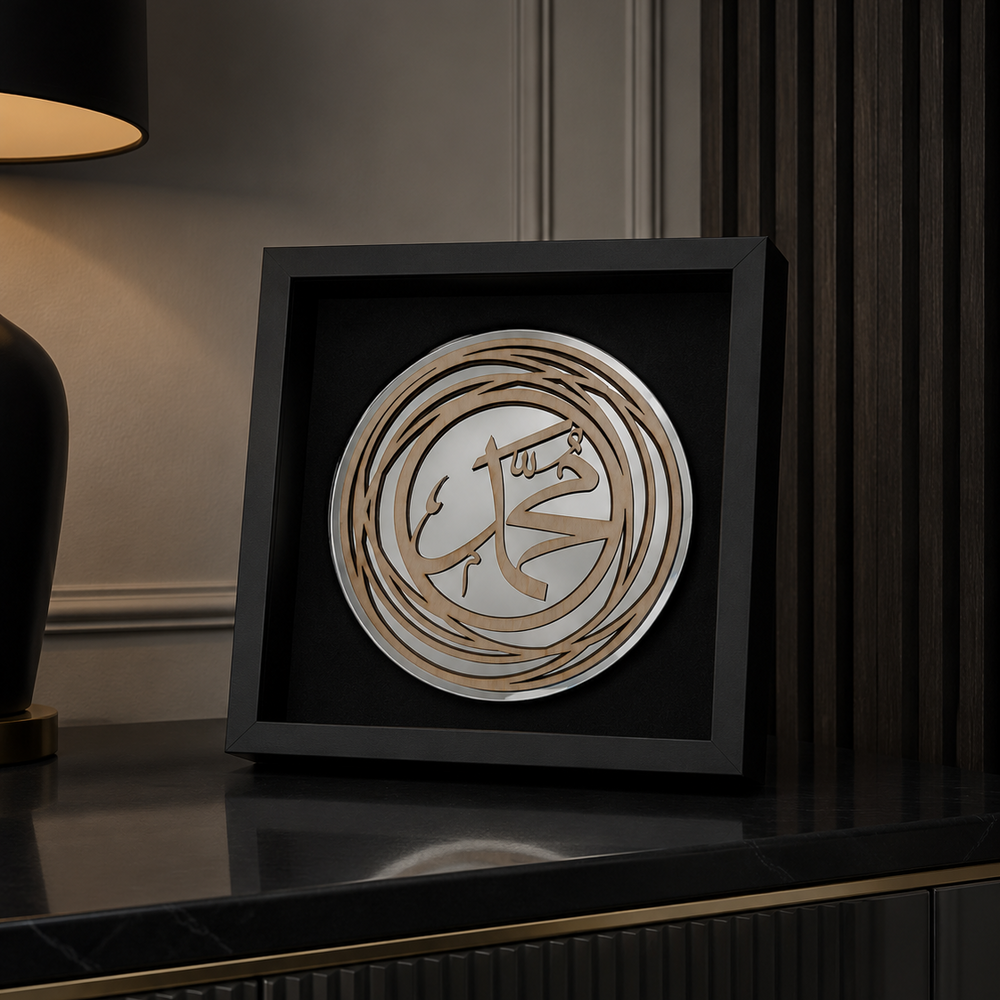 A square black shadow box frame containing a circular wooden calligraphy art piece, displayed on a dark glossy cabinet in a modern interior setting.