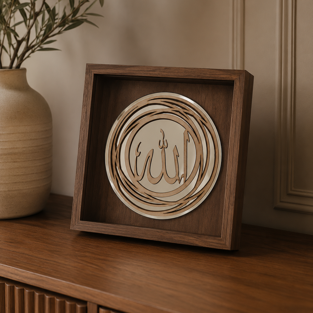 A square wooden shadow box display featuring layered circular wood cutouts with Arabic calligraphy, placed on a wooden cabinet next to a beige ceramic vase with green branches.
