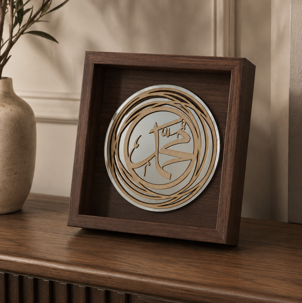 A square dark wood shadow box display featuring a circular layered wooden design with Arabic calligraphy, shown on a wooden console table next to a ceramic vase.
