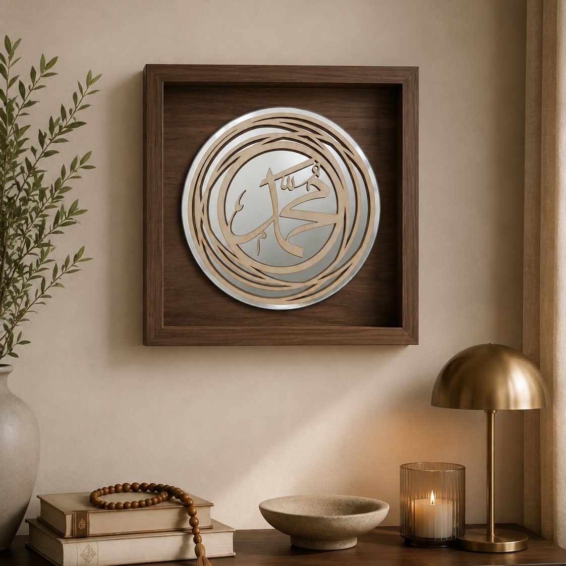 Square framed wall art featuring layered circular metallic and wood elements with an Arabic calligraphy motif, displayed on a beige wall above a wooden console with books, a bowl, a candle, and a brass lamp.